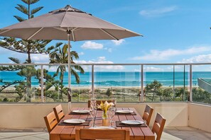 Comedor con mesa dispuesta para cuatro, con vista a una playa con palmeras y el océano.
