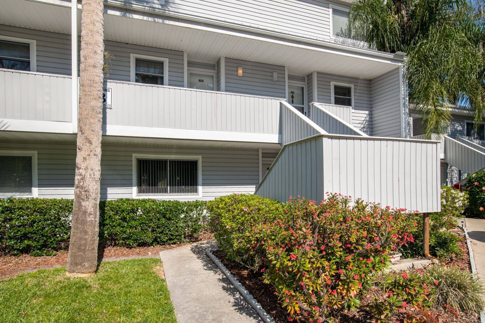 A multi-story residential building with a balcony on the second floor, a small porch area, and a well-maintained garden with various shrubs and flowering plants.