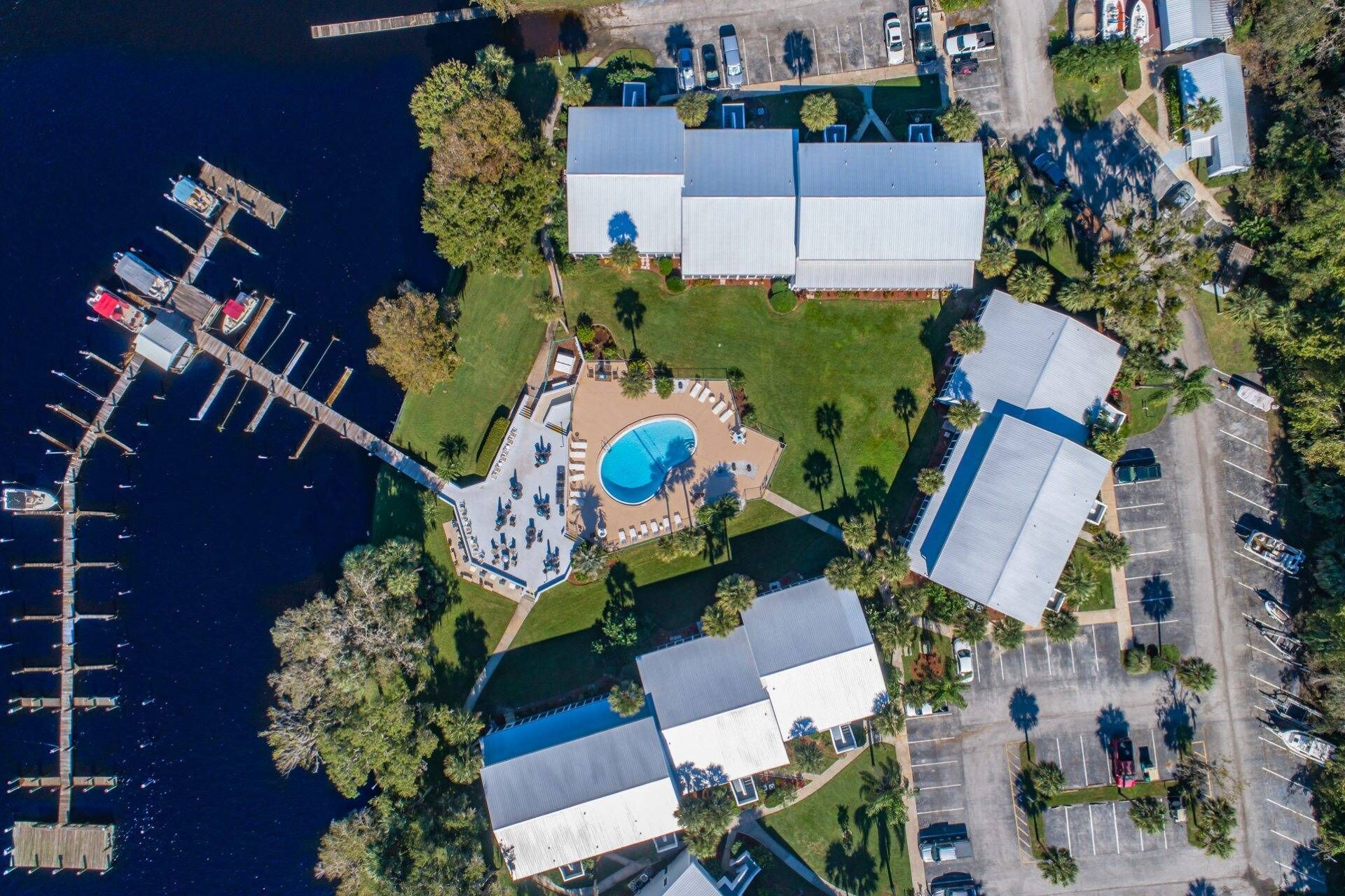 An aerial view of a marina with docked boats, a swimming pool, and several buildings with flat roofs.