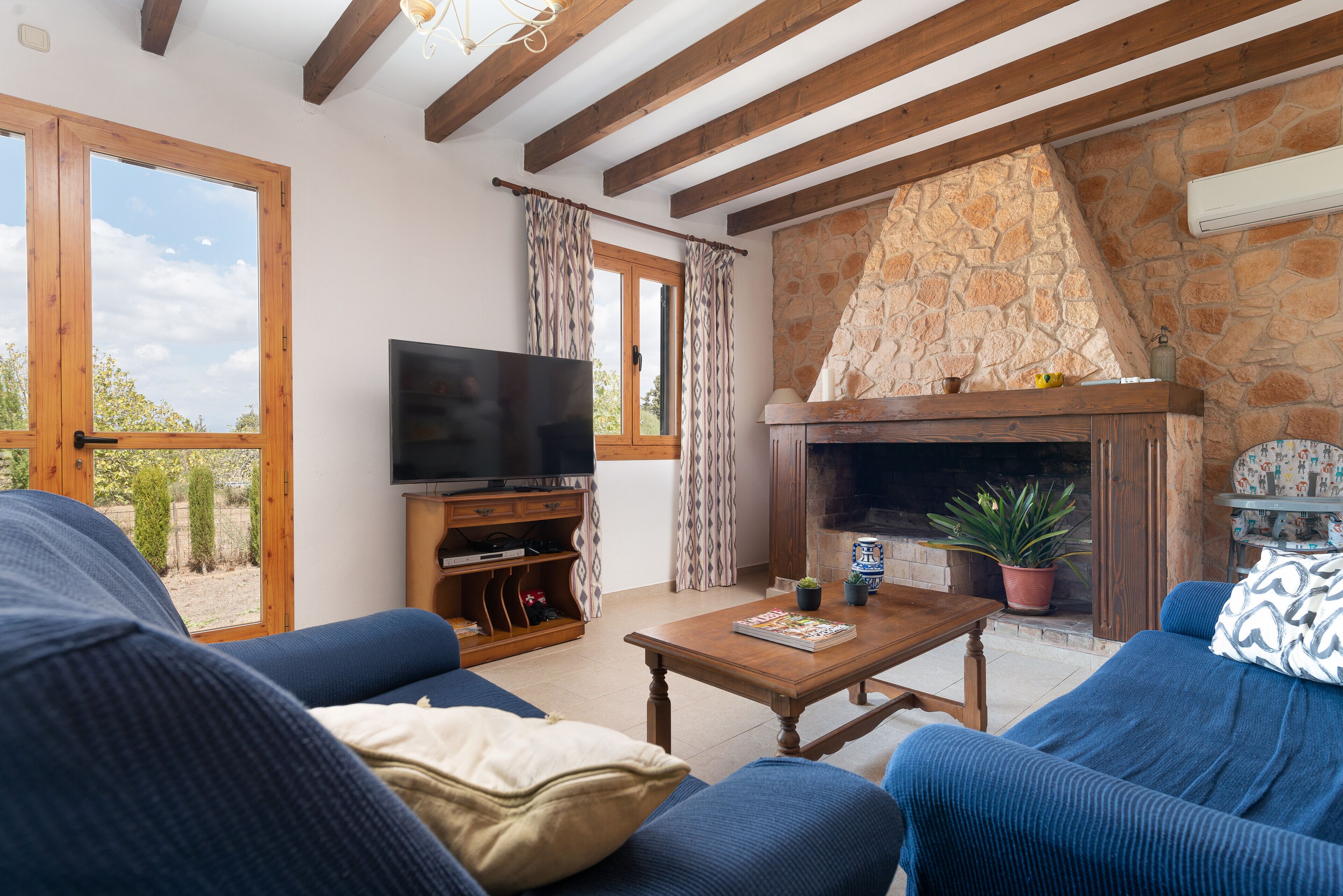 Una sala de estar con chimenea de piedra, vigas de madera, televisor y sofás azules.
