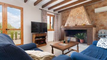 Una sala de estar con chimenea de piedra, vigas de madera, televisor y sofás azules.