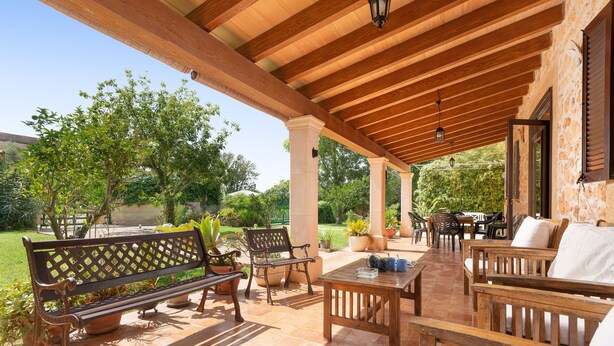 En udendørs terrasse med træmøbler, herunder bænke og borde, under en pergola med fliseterrasse.