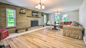 A spacious living room with a fireplace, a television mounted on the wall, and a large window providing a view of the outdoors. - Roomy Montour Falls Retreat w/ Private Pool! (Montour Falls)