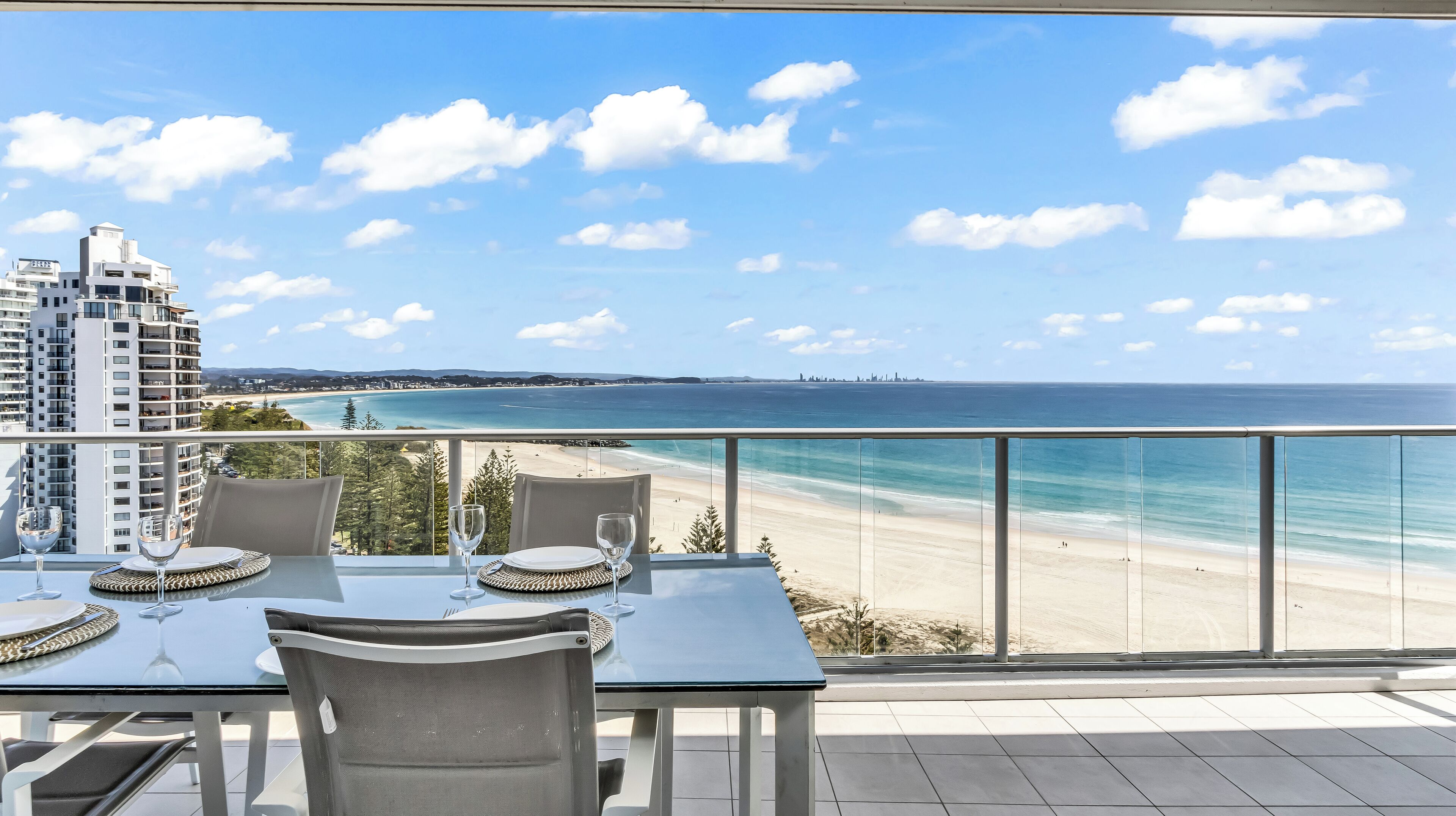 A balcony with a table set for two, overlooking a beach and ocean.