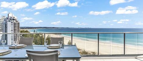 A balcony with a table set for two, overlooking a beach and ocean.