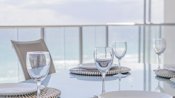 A dining table with clear glassware and woven placemats, set against a backdrop of a high-rise building and a clear sky. - Reflections 1501 - 3Bed with ocean views Newly Refurbished (coolangatta)