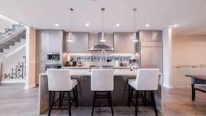 A modern kitchen with a central island, bar stools, pendant lighting, and a staircase leading to an upper level. - Luxury House in the heart of Old Town with Parking  (Chicago)