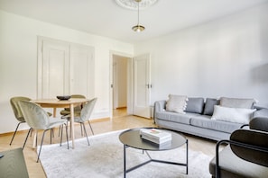 Un salon moderne avec un canapé gris, une table basse ronde et un coin repas comprenant une table et des chaises en bois.