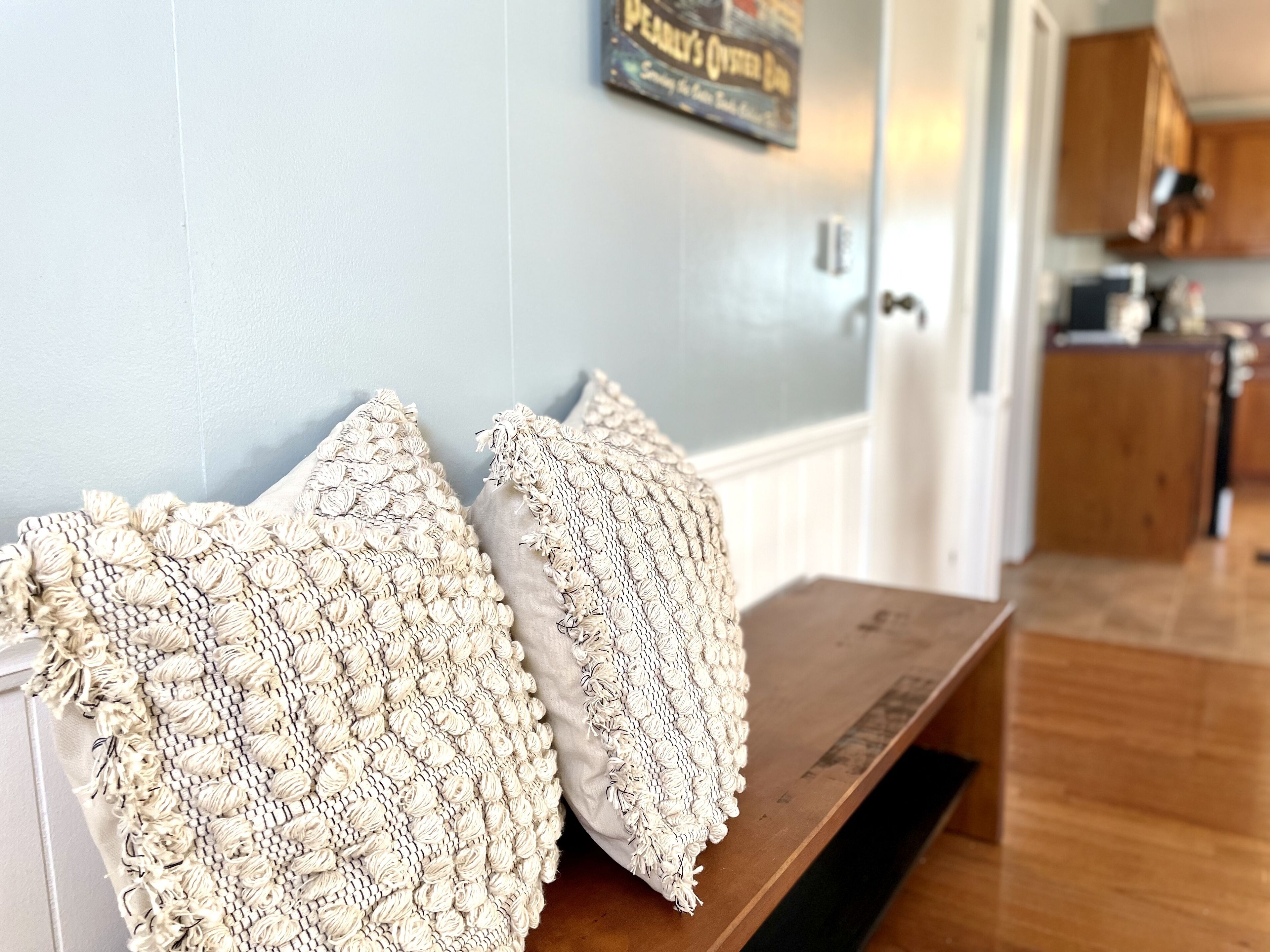A wooden bench with two textured pillows against a light blue wall.