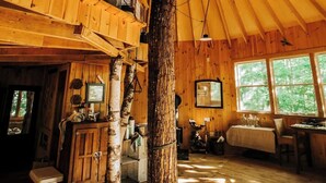 A spacious wooden interior with a large central column, wooden beams on the ceiling, and a dining area with a table and chairs. - Island Tree House Glamping (Monmouth)