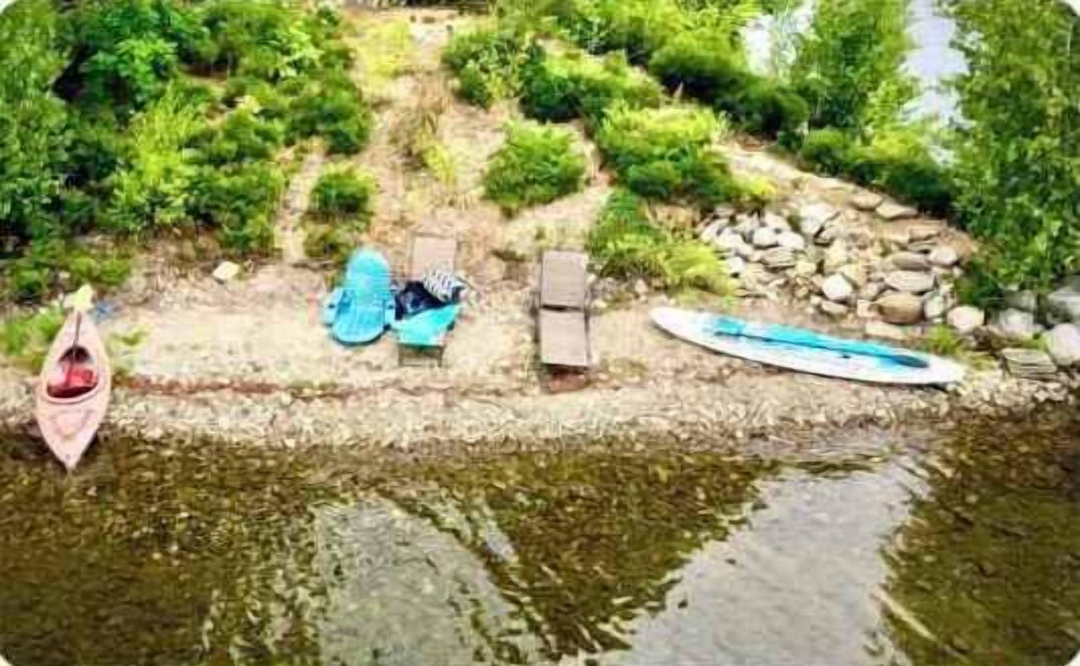 Een waterpartij met een kano, een paddleboard en een ligstoel aan het water.