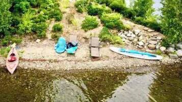 Een waterpartij met een kano, een paddleboard en een ligstoel aan het water.