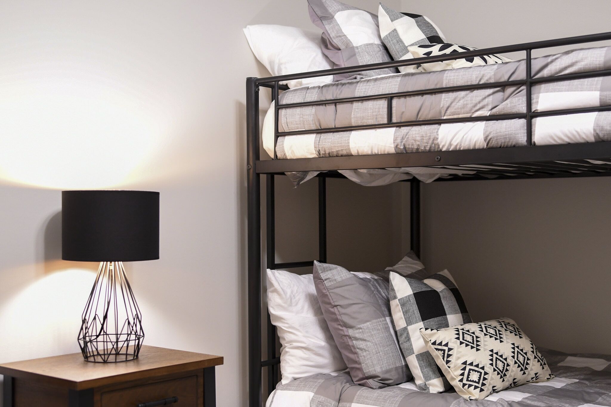 A bunk bed with a black metal frame, a bedside table with a lamp, and pillows with geometric patterns.