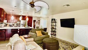 A modern living room with a sofa, ottoman, and a coffee table. There is a kitchen area with a refrigerator and a bar counter. - Downtown Tempe House Beauty with yard! Mill 3 blocks. ASU half mile.  (Tempe)