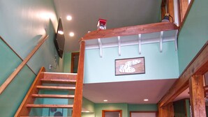 A wooden staircase leading to a loft area with a wooden railing, a white door, and a framed artwork on the wall.