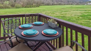 A round table with turquoise plates and a potted plant, set on a wooden deck with a view of a green field and hills.