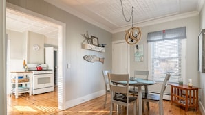 Un comedor con mesa y sillas de madera, una cocina al fondo y un techo con una lámpara decorativa.