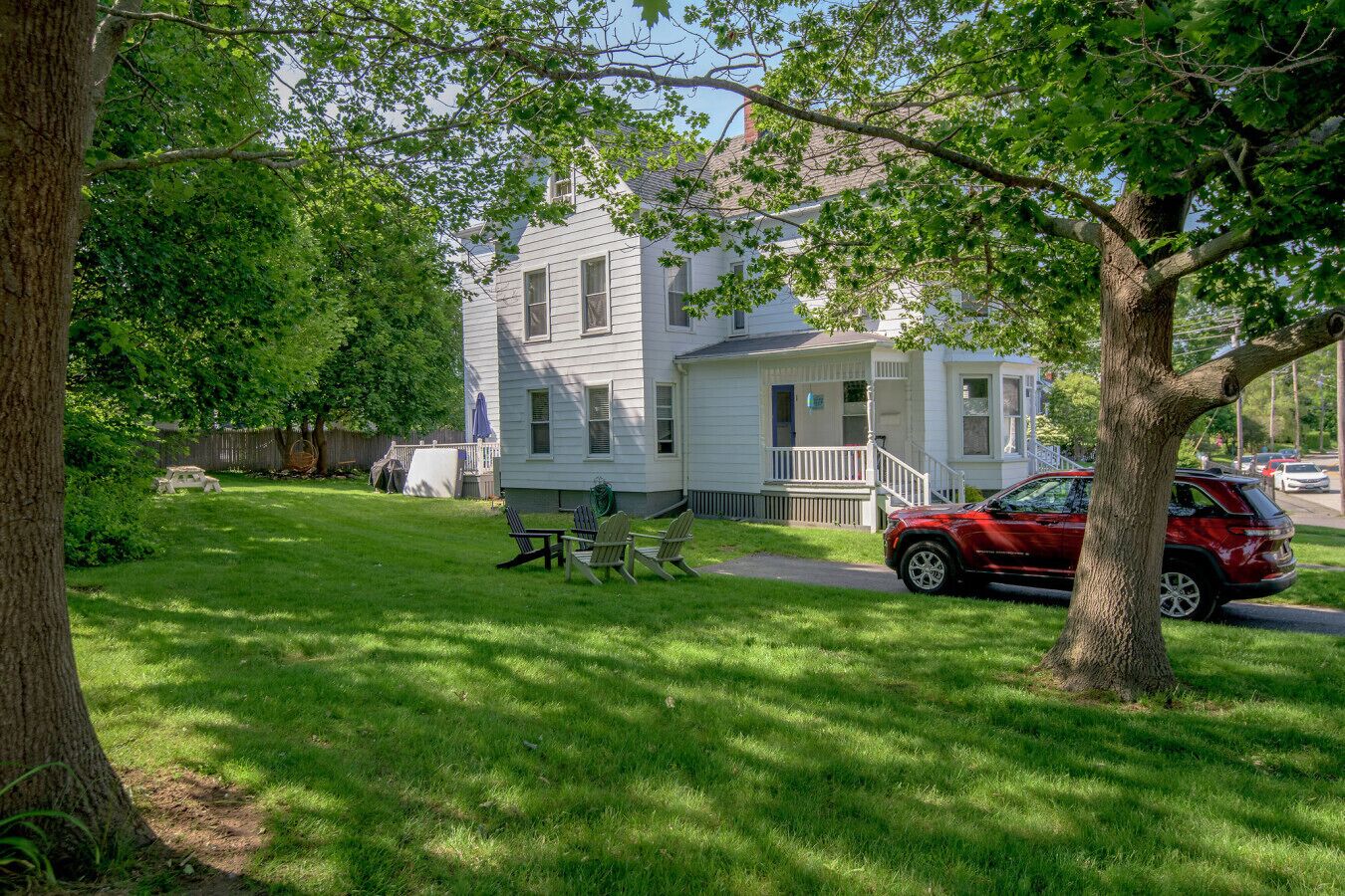 A two-story house with a front porch, a lawn, and a red SUV parked in front.