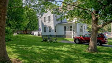 A two-story house with a front porch, a lawn, and a red SUV parked in front.