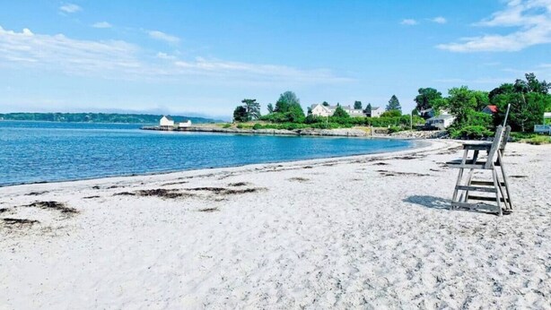 Una playa con una silla de madera y un edificio pequeño al fondo.