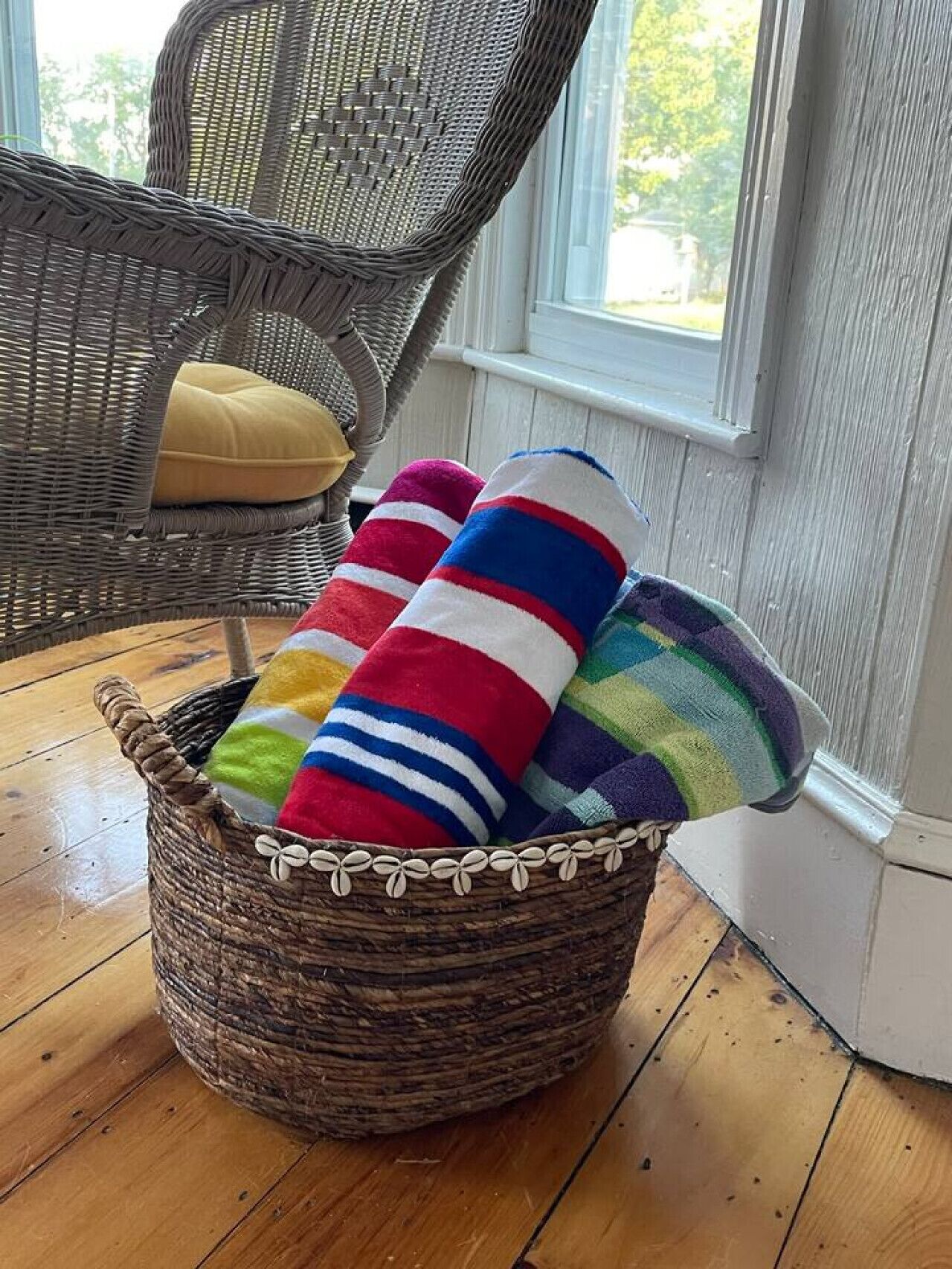 Una silla de mimbre con un cojín, una cesta de mimbre con toallas de rayas coloridas y un suelo de madera.