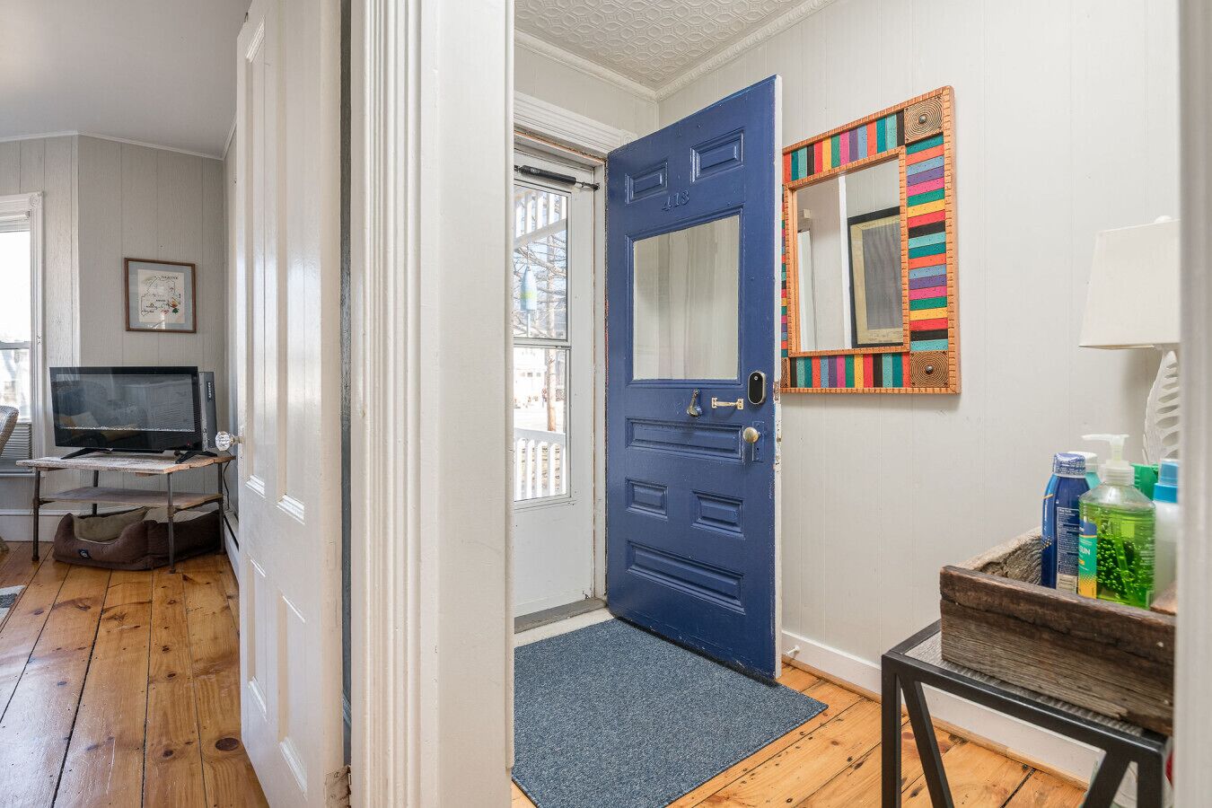 A room with a blue door, a television on a stand, a small table with toiletries, and a window with a view of the outside.