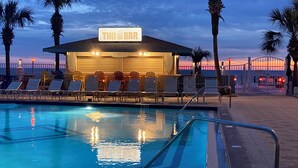 A tiki bar with a pool, lounge chairs, and palm trees. - SUNRISE /SUNSET GULF VIEWS #932 - FREE BEACH CHAIRS!!!!! (Panama City)
