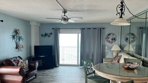 A living room with a TV, a ceiling fan, a dining table with chairs, and a balcony with curtains. - SUNRISE /SUNSET GULF VIEWS #932 - FREE BEACH CHAIRS!!!!! (Panama City)