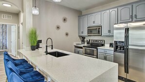 A modern kitchen with a large island, stainless steel appliances, and blue bar stools. - Vista Cay Resort Condo ~ 5 Mi to Universal! (Orlando)