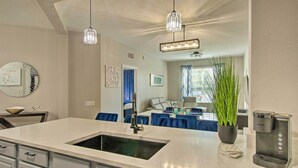 A modern kitchen with a central island, a coffee machine, and a dining area with blue chairs. - Vista Cay Resort Condo ~ 5 Mi to Universal! (Orlando)