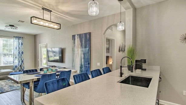 A modern kitchen with a large island, bar stools, pendant lighting, and a dining area with a TV. - Vista Cay Resort Condo ~ 5 Mi to Universal! (Orlando)