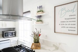 A kitchen with white cabinets, a microwave, a gas stove, and a framed quote on the wall.