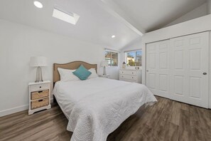 A bedroom with a bed, nightstands, a dresser, a white door, and a skylight. - Charming Hillcrest/Mission Hills 3 BR + House (San Diego)