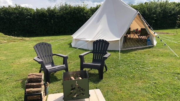 Une tente avec une table et des chaises installées sur un terrain herbeux.