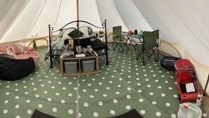 L’intérieur d’une tente comprenant un lit, une table avec des chaises et un espace de repos avec un fauteuil poire.