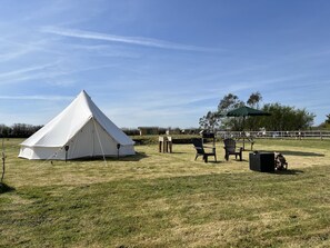 Una carpa blanca, dos sillas Adirondack, una mesa y un paraguas verde en un campo cubierto de hierba.