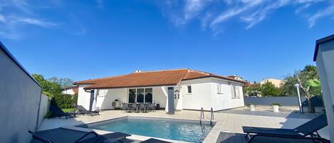 A poolside area with a swimming pool, lounge chairs, and a building with a tiled roof.