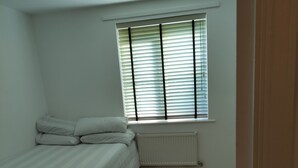 A bedroom with a bed, a radiator, and a window with blinds. - Immaculate 1-Bed Apartment in Borehamwood (Borehamwood)