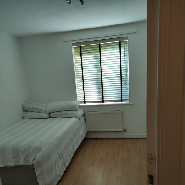 Een slaapkamer met een bed, een radiator en een raam met zonwering.