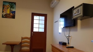 A room with a bed, a wooden desk, a chair, a television mounted on the wall, and a door with frosted glass panels. - Caye Caulker Beach Hotel (Caye Caulker)