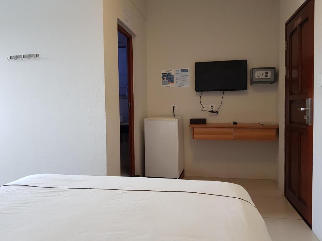 Ein Hotelzimmer mit einem Bett, einem kleinen Kühlschrank, einem an der Wand befestigten Fernseher und einem Holzschrank darunter.