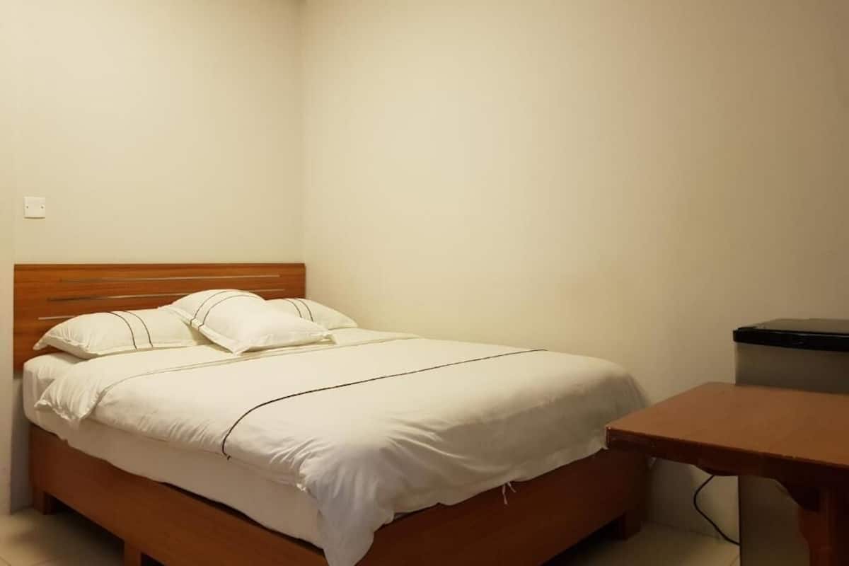 Een enkel bed met houten hoofdeinde, een nachtkastje en een prullenbak.
