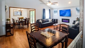 A living room with a wooden dining table, a sofa, a TV, and a ceiling fan.