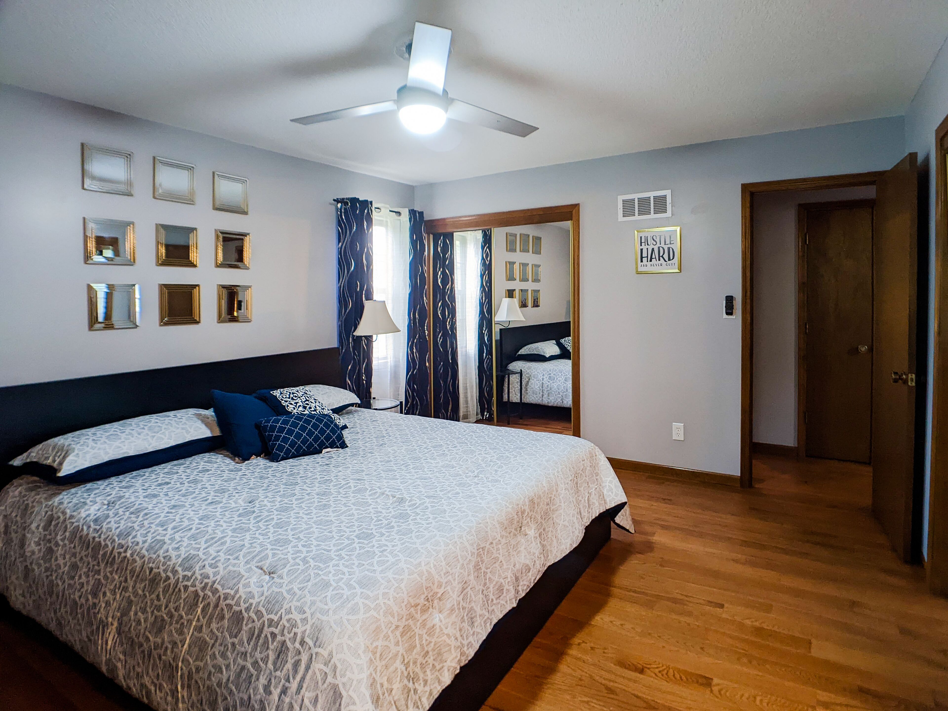 Une chambre avec un grand lit, un ventilateur de plafond et une porte donnant sur une autre pièce.