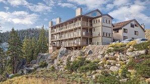 A multi-story building with a balcony on the ground floor, surrounded by a rocky hillside and forest.