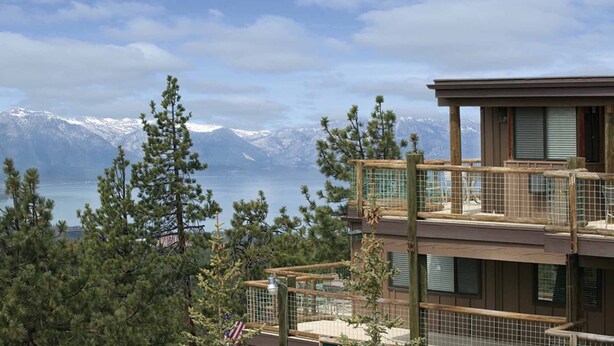 A modern building with a balcony overlooking a mountainous landscape and a body of water.