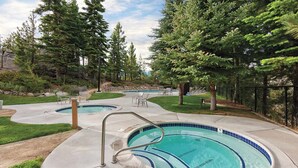 A swimming pool area with multiple pools, surrounded by trees and a stone wall.
