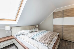 Un dormitorio con techo inclinado, una cama con ropa de cama a rayas, una mesita de noche con lámpara y un armario con paneles de madera.
