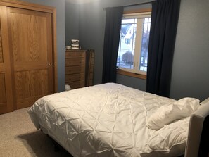 Un dormitorio con una cama grande, un aparador, una ventana con cortinas y una puerta.