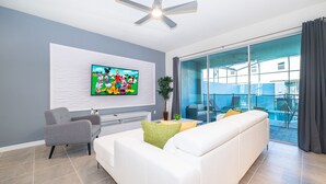 A modern living room with a white sofa, grey armchair, and a flat-screen TV mounted on the wall. - AL1802 Solara Resort 5 Beds 4.5 Baths Private Pool & Free Waterpark (Kissimmee)